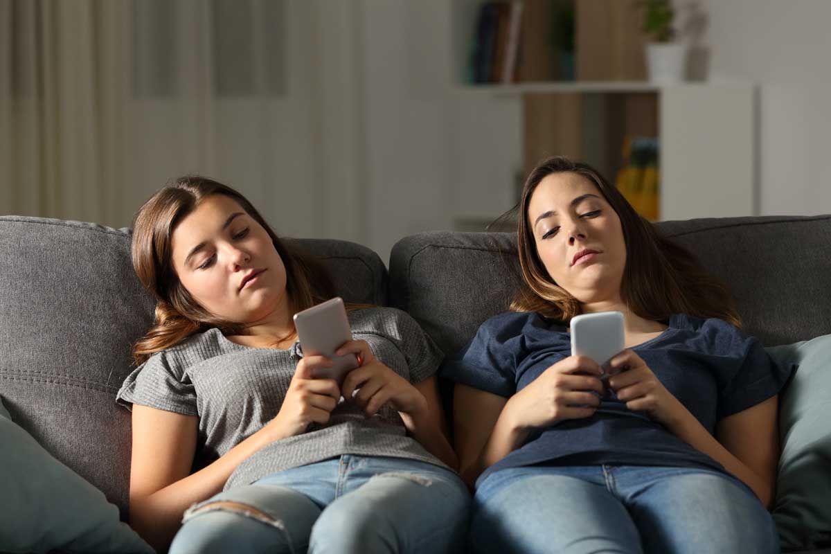 two bored teenage girls look at their phones