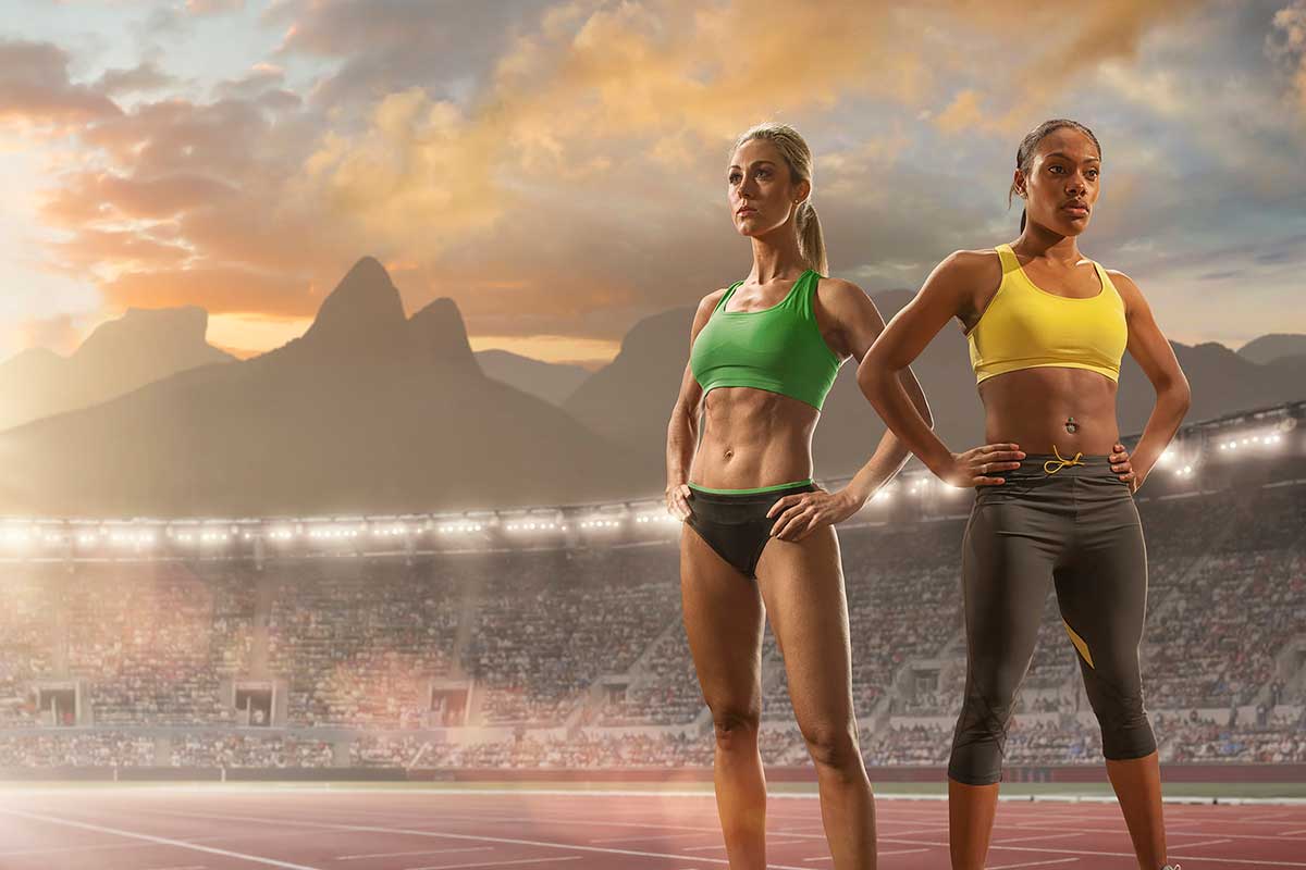 Two female athletes standing on a track in a stadium.