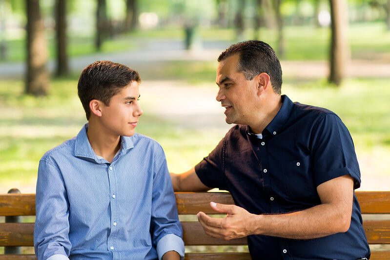 A father and son sitting on a bench talking to each other