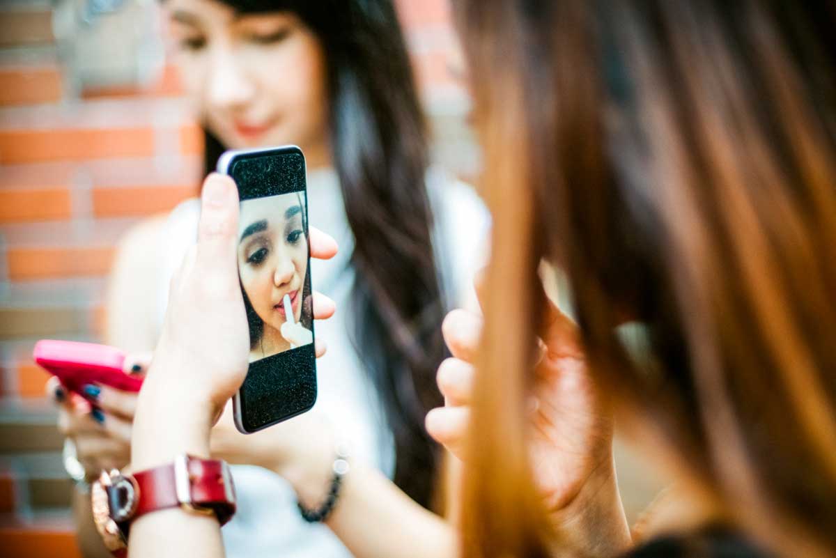 Teen girl uses phone while putting on makeup