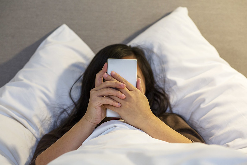 A young girl is looking at a mobile phone in bed. 