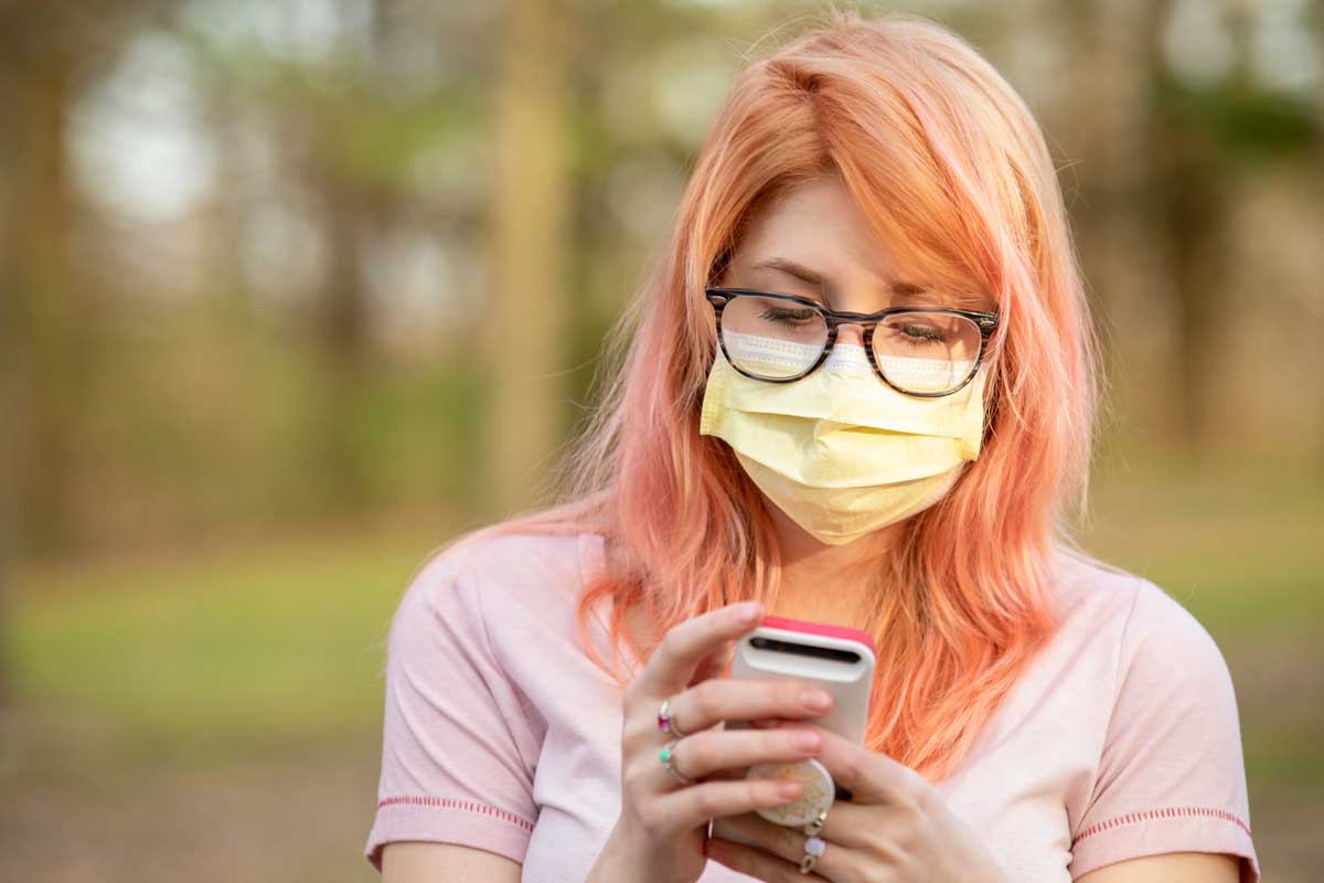 Teen girl wearing mask looks at smartphone.