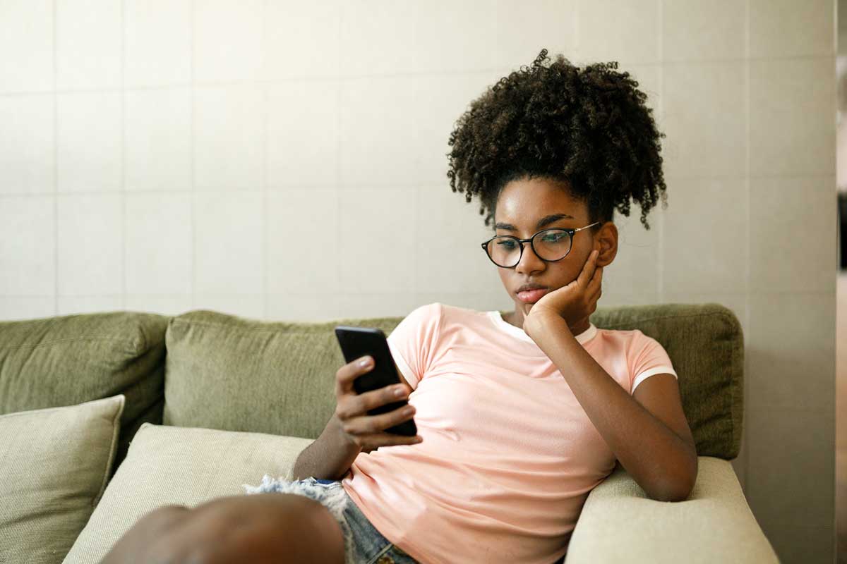 Teenage girl sits on couch and stares at smartphone screen