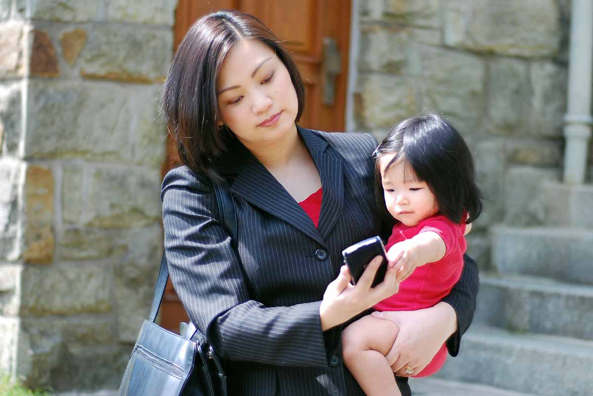 Business woman looks at cellphone while holding baby
