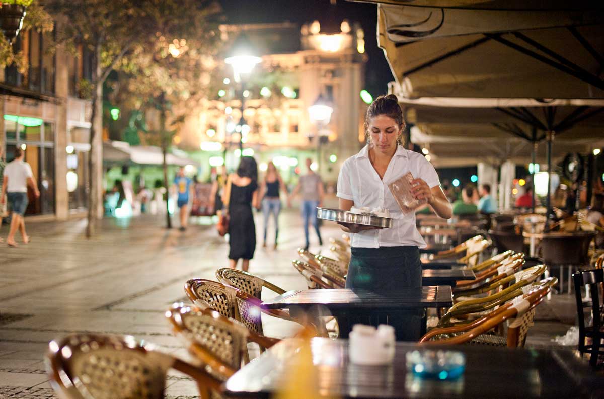 A woman working as a server clears an outdoor cafe table.
