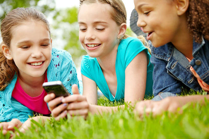 Three little girls spending time together and sharing a smartphone while outdoors.
