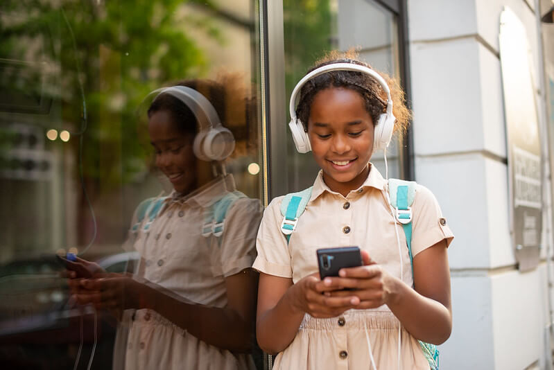 A child wearing headphones using her smartphone.