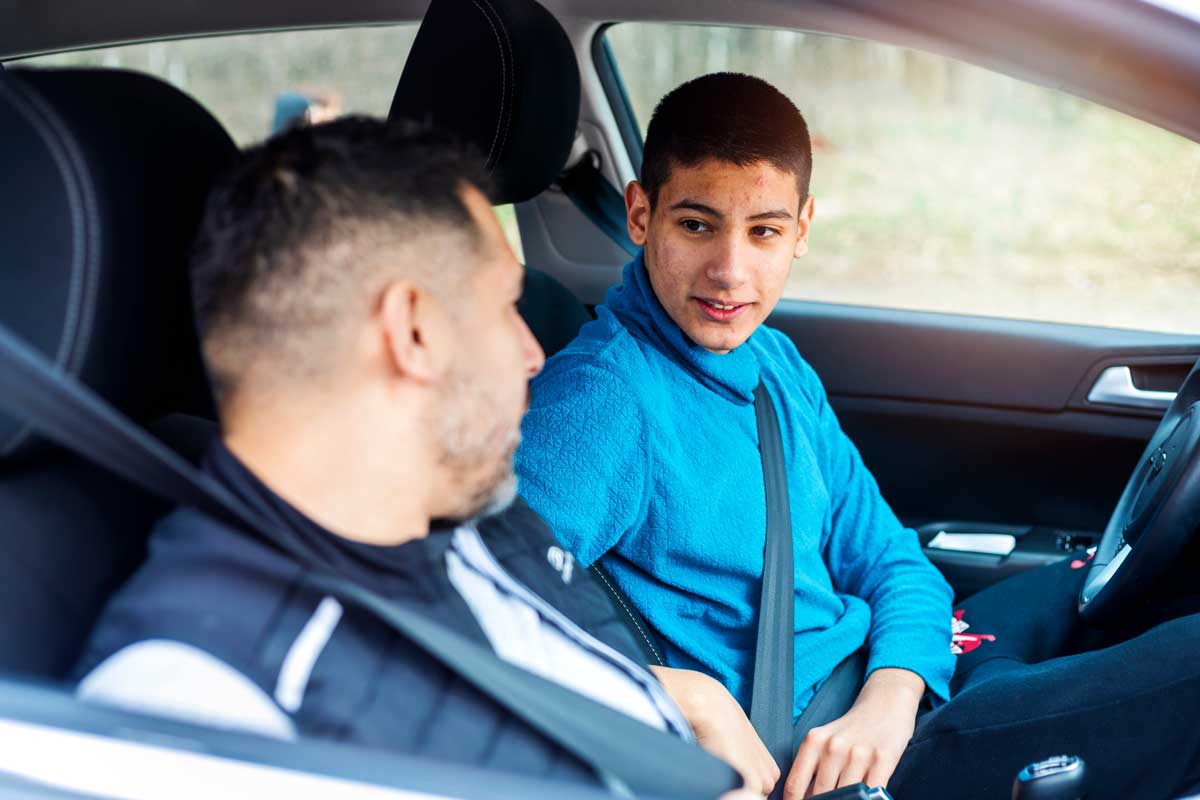Father talks to his teenage son while sitting in a car