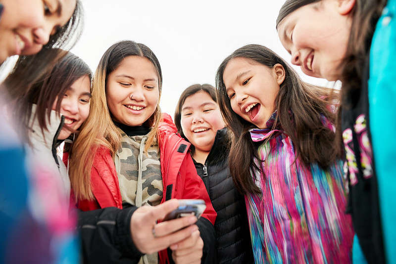This photo shows a group of girls looking at mobile phone and smiling.
