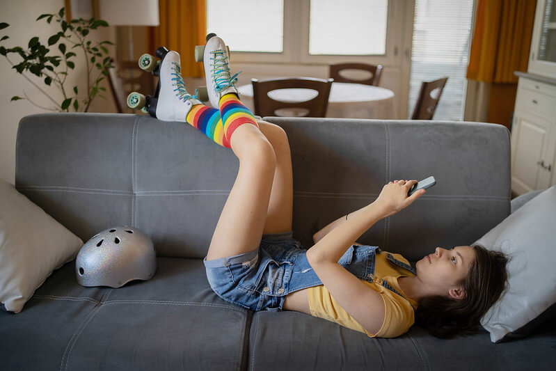 A teenage girl using her phone while lying on a sofa