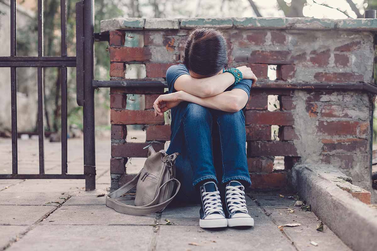 Sad teen girl sitting on the ground with head in hands