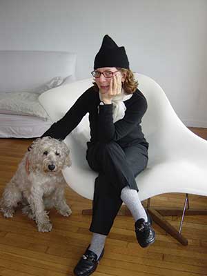 Maira Kalman sitting in a chair with a dog next to her